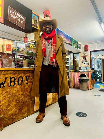 Emeka Kuizhi Otagburuagu, founder of Black Cowboy Coffee stood in front of the coffee macine wearing a cowboy hat and boots